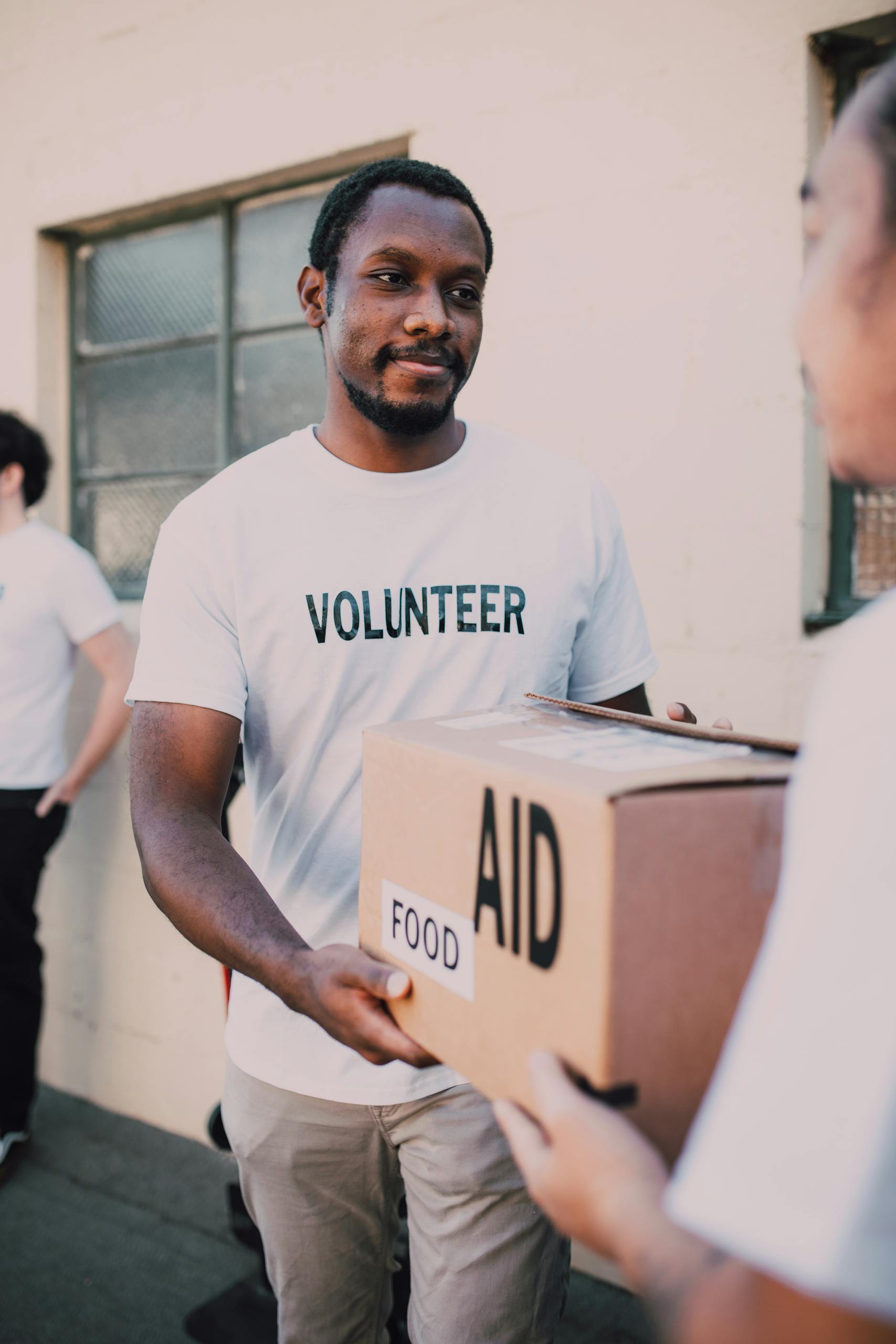 A volunteer hands a box labeled 'aid' and 'food' during an outdoor charity event.