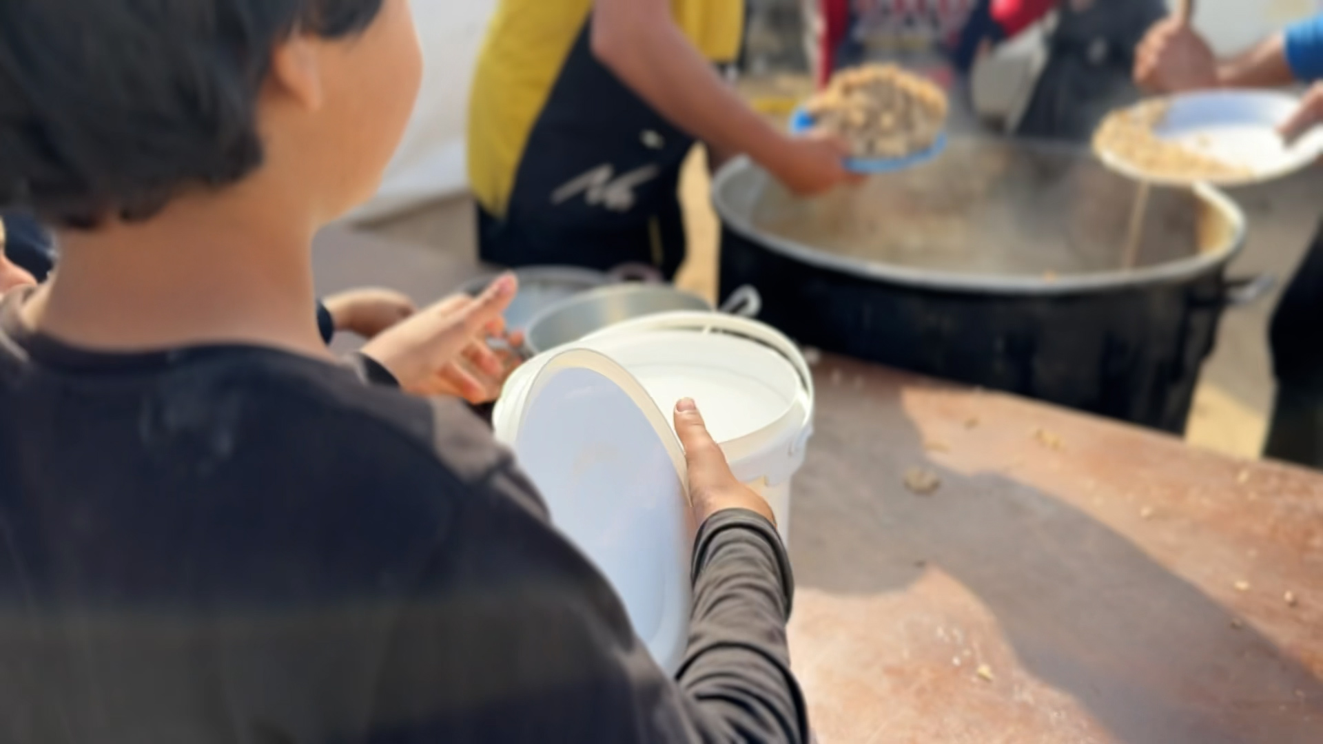 A child holds out containers as hot food is served at a community kitchen in Gaza
