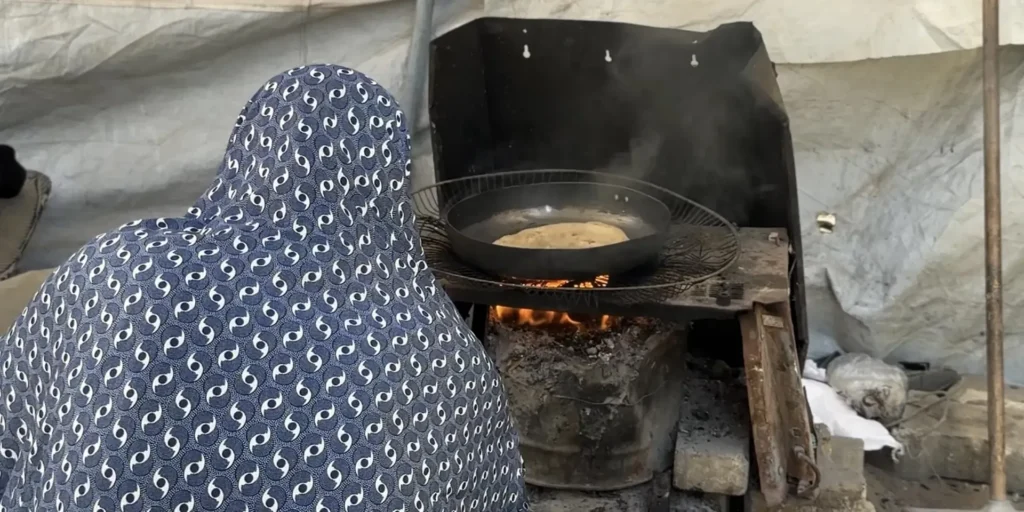 A mother bakes flatbread over a wood fire outside her tent in Gaza