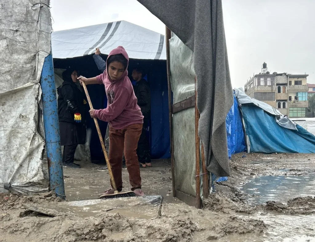 A girl sweeps mud away from the entrance of her family’s tent after rain in Gaza